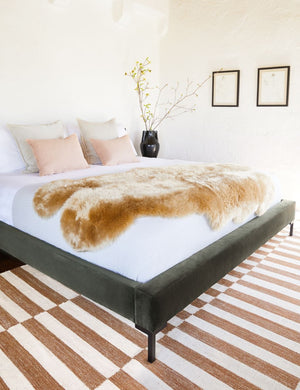 The Deva Deva Moss platform bed lays in a bedroom with a sheepskin atop a striped rug