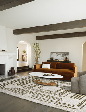 The Earth Maze Moroccan Shag Rug lays in a living room under an oval coffee table and cognac velvet sofa