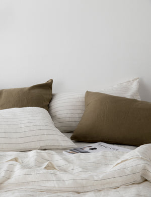 The Set of two european flax linen olive green pillowcases by cultiver lay on a bed with pencil stripe cultiver linens
