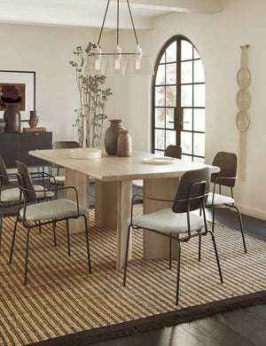 The Sun at six crest white oak dining table with curved legs sits in a dining room with metal dining chairs, brown sculptural vases, and a striped brown and beige rug