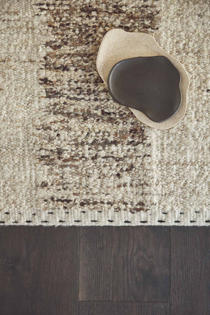 Bird's-eye view of the esha rug laying on a dark wooden floor with a beige speckled bowl and black bowl sitting atop it