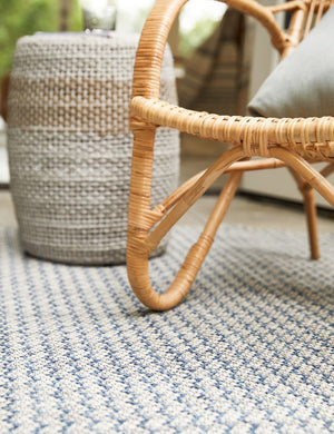 Close-up of the Sonya gray and blue geometric indoor and outdoor rug in an outdoor space with woven and jute furniture sitting atop it