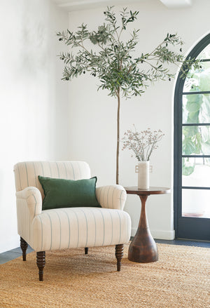 The Darby side table sits in the corner of a room atop a jute rug next to a cream striped accent chair