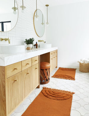 The Arches rust orange Rug in its runner size lays on a circle-tiled bathroom floor next to double sinks with round mirrors