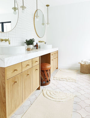 The Arches natural Rug in its runner size lays on a circle-tiled bathroom floor next to double sinks with round mirrors