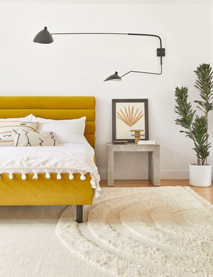 The Arches natural Rug lays in a bedroom under a golden velvet framed bed and next to a stone night stand