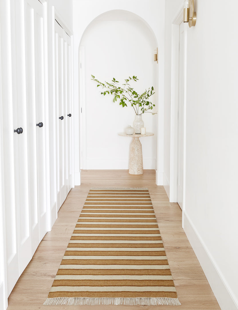 #size::2-6--x-8- | The elane rug in its runner size lays in a white hallway with an arch and a natural stone side table with three white vases