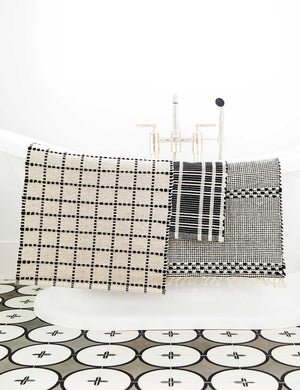 The Masha gray and black geometric machine washable mat is draped over a white bathtub with other bath mats
