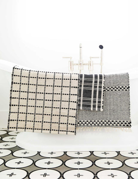 #size::1-9--x-2-10- #size::2--x-5- | The Masha gray and black geometric machine washable mat is draped over a white bathtub with other bath mats