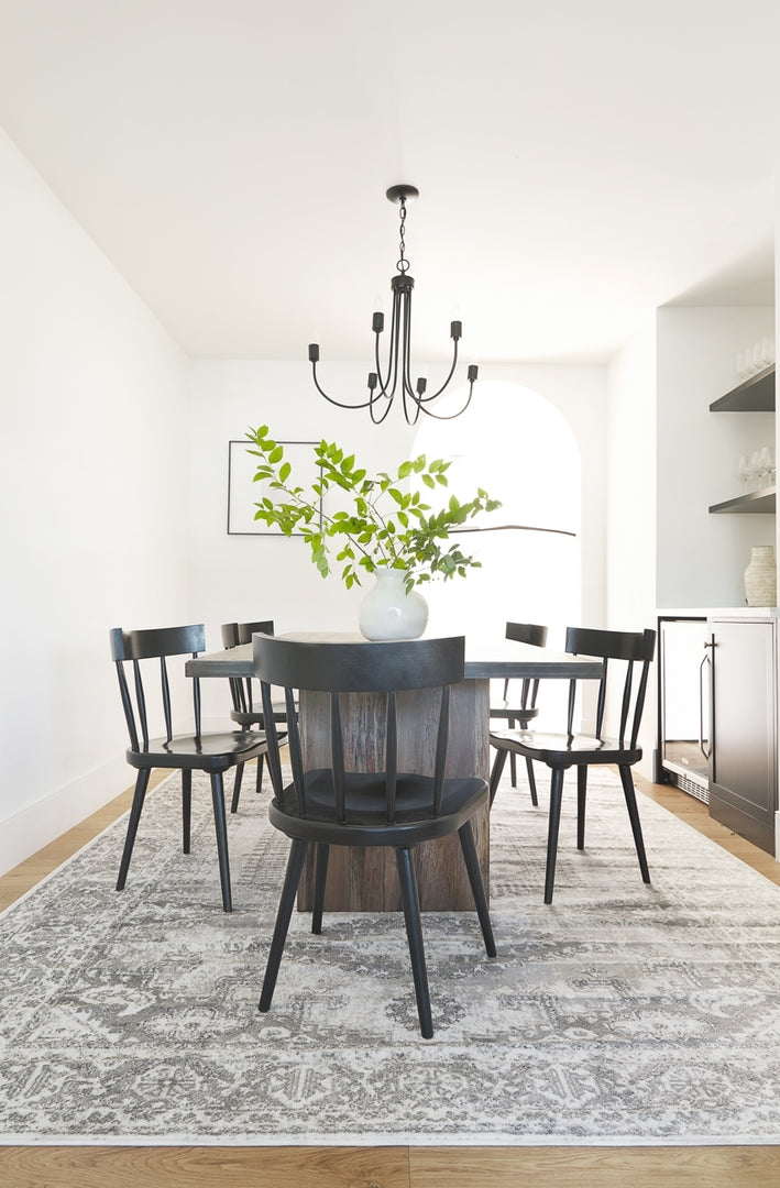 | Five Neema black mahogany dining chairs surround a dark wooden dining table, all sitting atop a gray and black persian rug.
