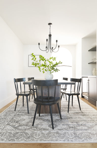 | Five Neema black mahogany dining chairs surround a dark wooden dining table, all sitting atop a gray and black persian rug.