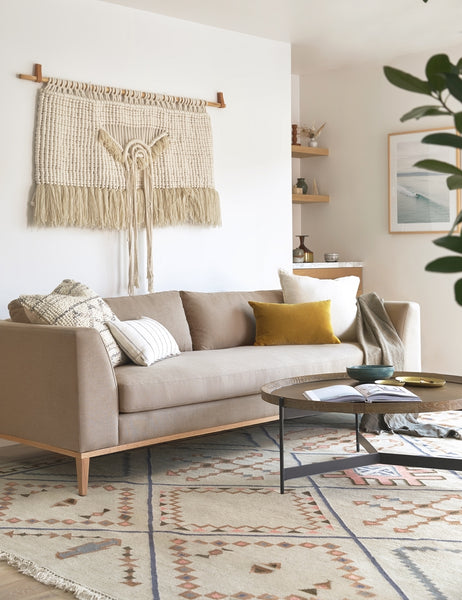 #size::10-w #size::6-w #size::7-w #size::8-w #color::pebble #size::9-w | The Charleston pebble gray linen sofa sits under a woven wall hanging atop of an ivory rug with a diamond patterned design