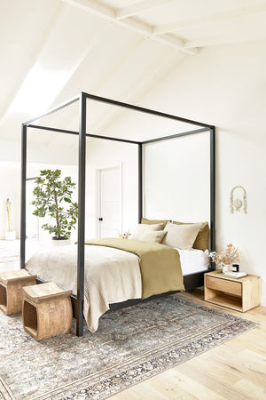 Two devlin stools sit atop a traditional rug in a bedroom at the edge of a black-framed canopy bed