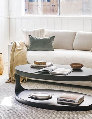 Charlotte moss green velvet lumbar pillow sits on a cream couch next to an oval coffee table