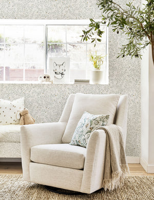 The Dainty Leaves floral Wallpaper by Rylee + Cru is in a nursery with a natural linen swivel chair and a woven brown rug