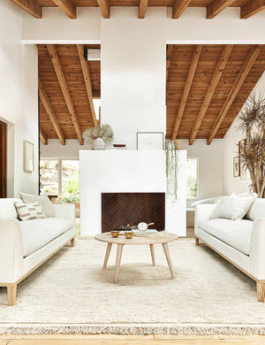 Two Charleston Ivory Linen sofas sit across from each other with a white fireplace and a round wooden coffee table