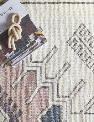 A close-up of the Zehra hand-knotted ivory, gray and purple medallion wool-blend area rug with a book and ceramic knot on top of it.