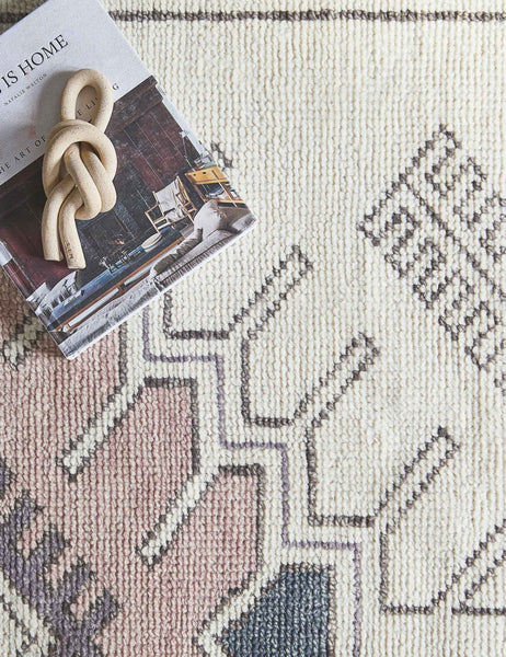 #size::2-6--x-8- | A close-up of the Zehra hand-knotted ivory, gray and purple medallion wool-blend area rug with a book and ceramic knot on top of it.