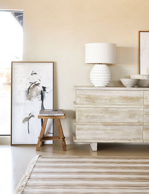 The Shauna neutral toned abstract wall art sits in a room with a natural striped rug, a whitewashed wooden sideboard, and a wooden stool