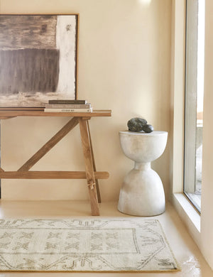The Rehya neutral geometric wool patterned rug sits in an entryway with a wooden sideboard, a natural toned wall art, and a sculptural white side table