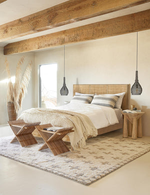 The Hannah bed with light wood cane bed frame sits in a bright bedroom with a plush patterned rug beneath it and wooden ceiling beams above it.