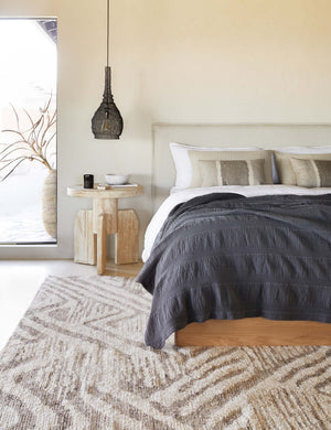 The Nantucket Cotton Matelassé midnight grey Coverlet by Pom Pom at Home lays on a natural linen framed bed in a bedroom with a black jute pendant light and patterend rug