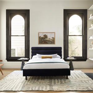 The braeburn rug lays in a bedroom under two black marble nightstands and a navy blue emerald framed bed