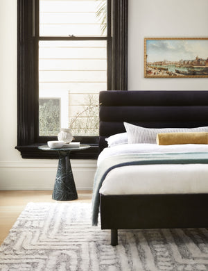 The Bailee Navy Velvet platform bed lays in a bedroom next to a black framed window atop a patterned rug