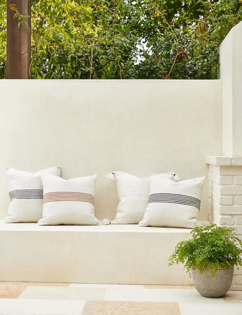 #color::black-stripe #color::rust-stripe  #style::square | Katya Indoor and Outdoor lumbar cream Pillow in all its colors sit together on a white bench outside