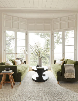 Two Jade Green Velvet Belmont Sofas sit opposite each other with an oval coffee table in between them in a room with floor to ceiling French doors