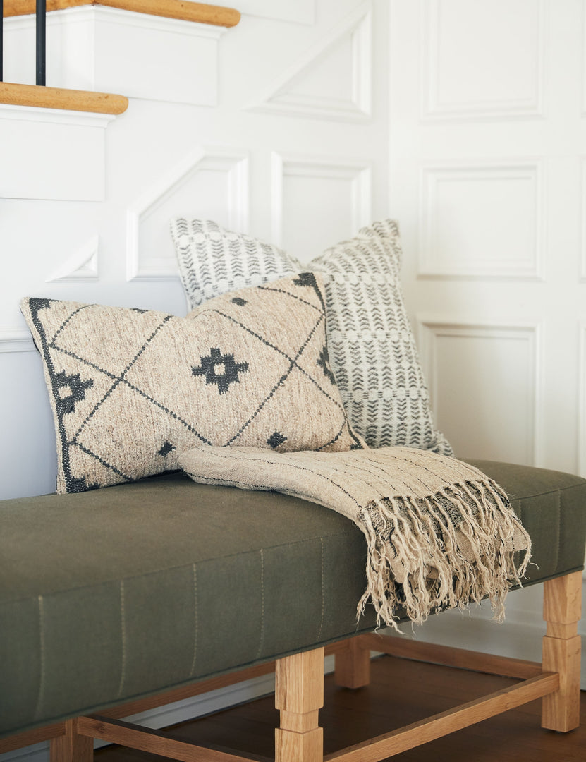 #insert::down #insert::polyester | The Nysa gray and white pillow with a woven geometric pattern sits atop a green cushioned bench behind a cream and gray patterned pillow