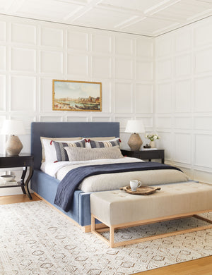 The Peregrine black and white marled striped lumbar pillow lays in a modern english inspired bedroom with a navy framed bed, a sand-toned bench, and white accented walls
