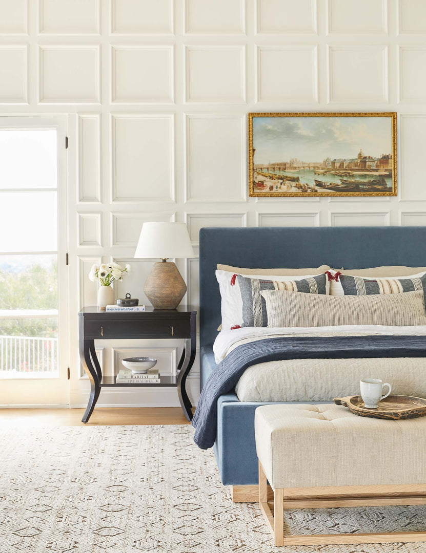 #color::harbor #size::cal-king #size::king #size::queen | The Lockwood blue velvet-upholstered bed with a white oak base sits atop a patterned hand-woven rug against a white, accented wall.