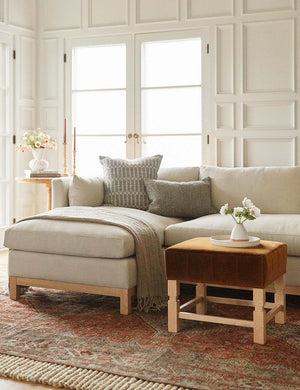 The Manon linen moss green lumbar boucle pillow sits on a natural linen sectional sofa in a living room with white accented walls