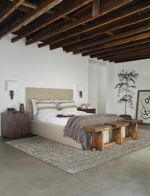 The Paxton flax linen slipcover bed sits in a room with wooden-beamed ceilings in between two accented wooden nightstands