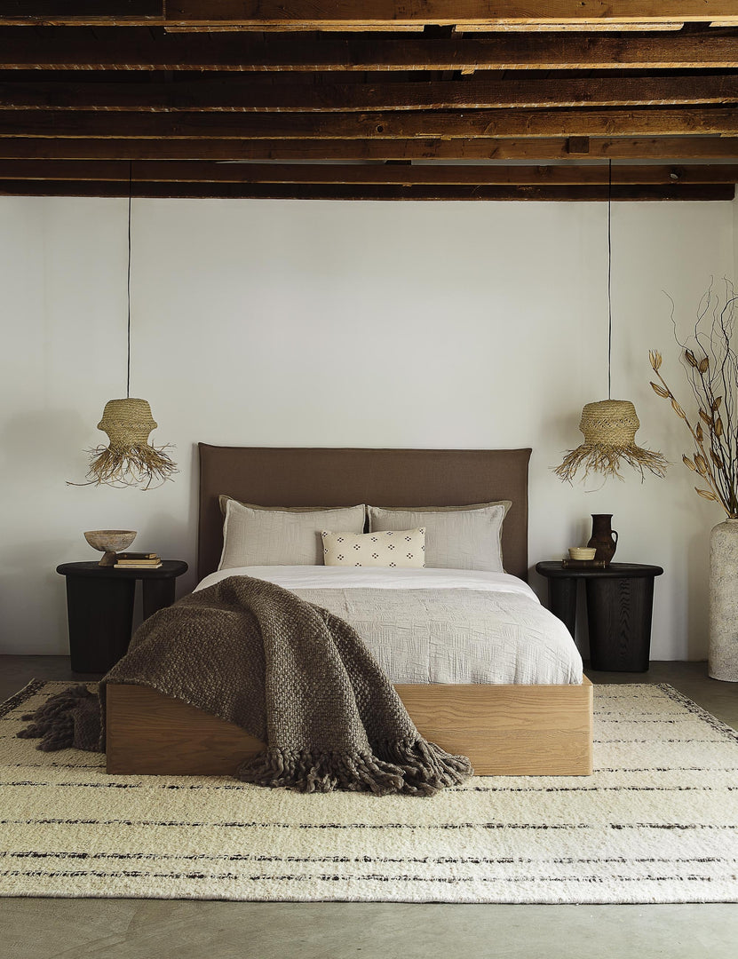 #size::king #size::queen #color::mushroom #size::cal-king | The Nia mushroom brown linen bed sits atop a plush rug in between two jute pendant lights under a wooden beamed ceiling