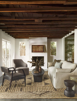 The Tobi gray boucle swivel chair sits in a rustic room with black and ivory furniture and wood-beamed ceilings