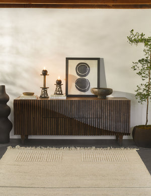 The Noemie Rug lays in a room in front of a wooden-textured sideboard with candles, wall art, and decorative bowls sitting atop it