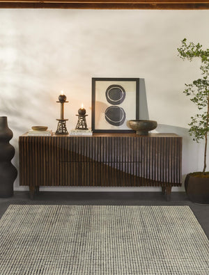 The Uma black and natural checkered grid pattern rug lays in a room with a paneled wooden side board