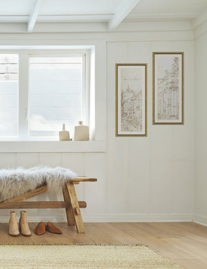The set of two Da Vinci diptych drawing prints are hung against a white accented wall in an entry way with a wooden bench