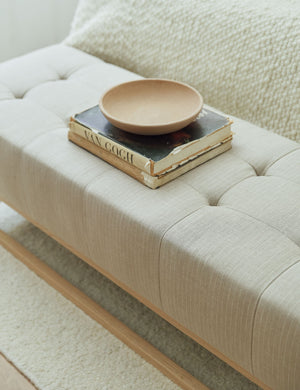 The Grasmere natural stripe linen wooden bench sits at the end of a neutral-toned with a bowl and stack of books atop it