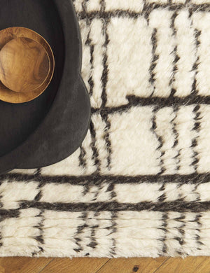 The Nora Moroccan Rug sits under a large black wooden tray and two smaller natural wooden bowls