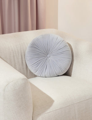 The Monroe ice blue velvet round pillow sits on a white accent chair