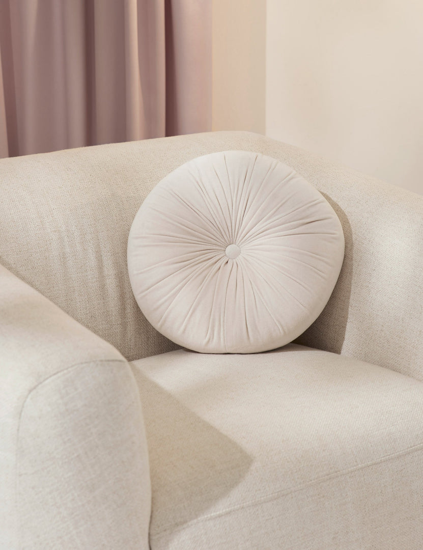 #color::oyster | The Monroe oyster white velvet round pillow sits on a white accent chair 