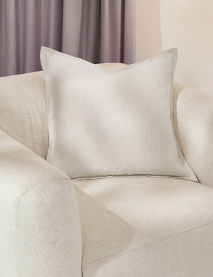 The arlo ivory square pillow sits in a studio room on a white linen accent chair