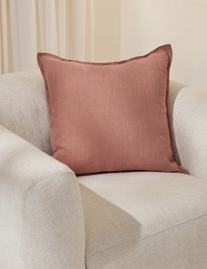 The arlo terracotta square pillow sits in a studio on top of a white linen accent chair