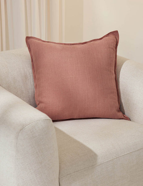 #color::terracotta #style::square | The arlo terracotta square pillow sits in a studio on top of a white linen accent chair