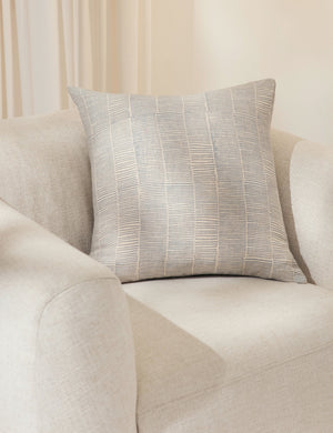 The claudette blue square pillow sits in a studio room atop an ivory linen accent chair
