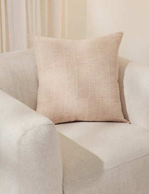 The claudette blush square pillow sits in a studio room atop an ivory linen accent chair