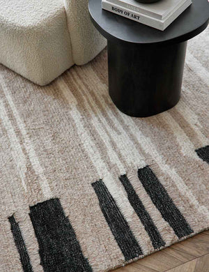Close up view of the gareth rug laying under a round black wooden side table and a cream boucle accent chair